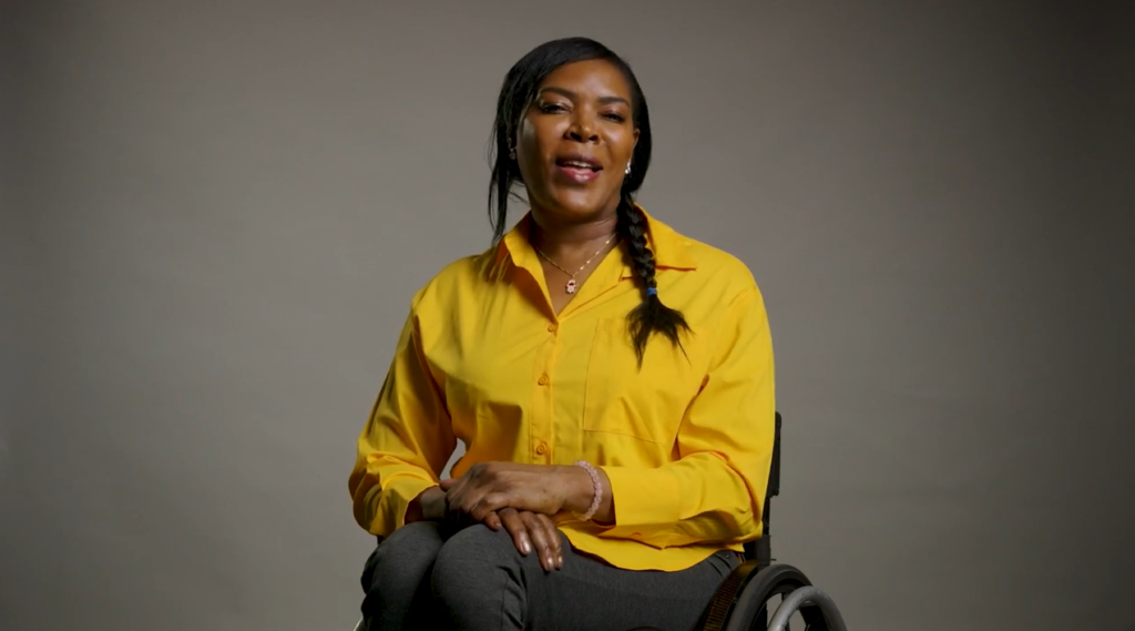 A woman in a wheelchair speaks to the camera