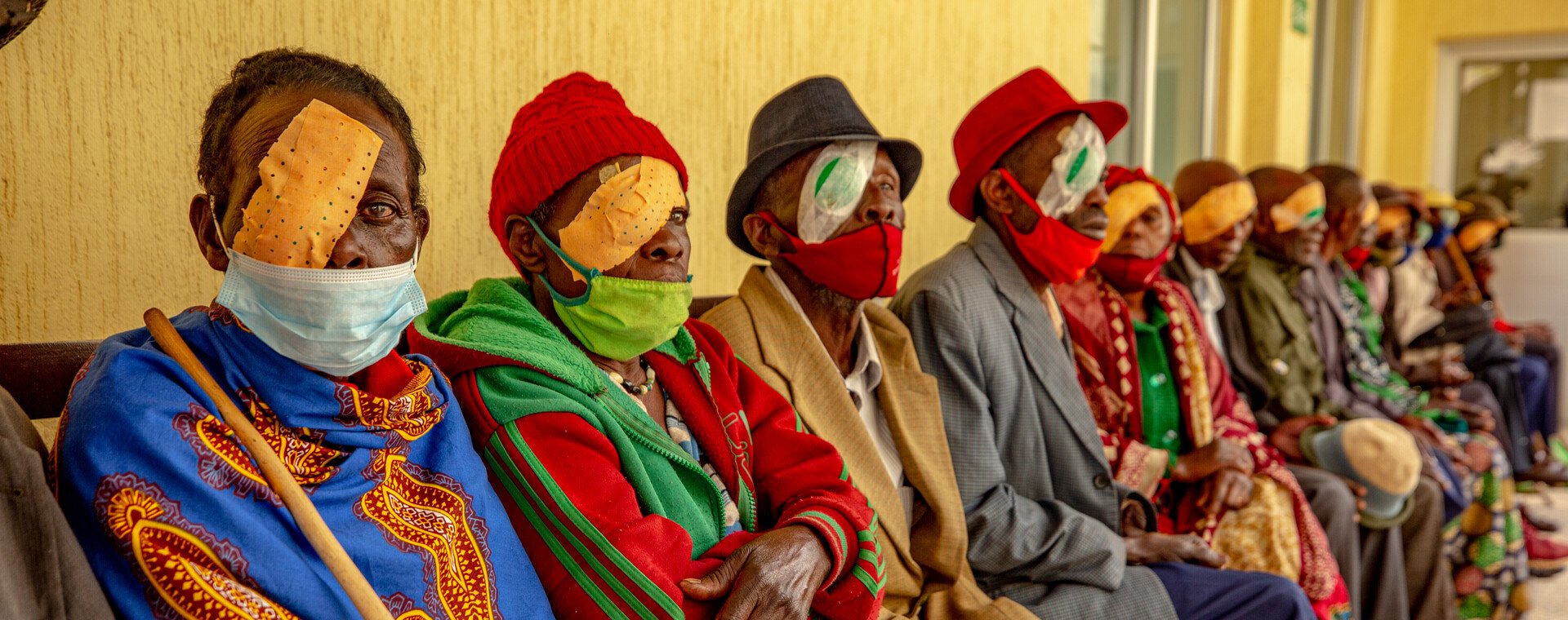 A group of people sit with green eye patches and tape on.