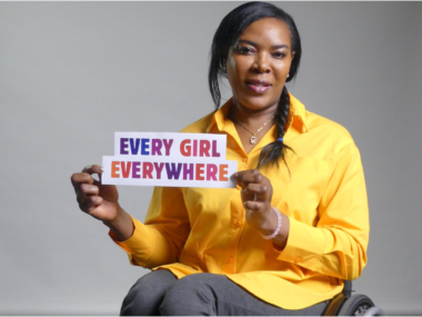 Anne Wafula Strike, wearing yellow, holding a sign saying Every Girl Everywhere.
