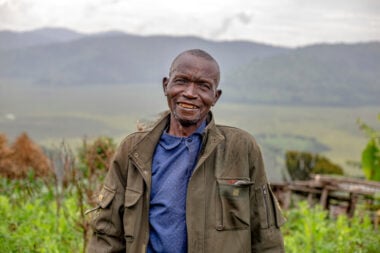 Cyprien smiles, standing outdoors with mountains in the distance