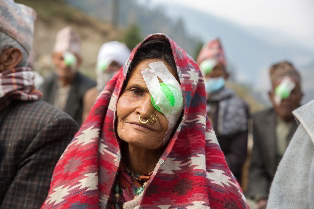 Jayakaunra, wearing a red headscarf, looks into the camera. On her left eye is a green patch following cataract surgery.