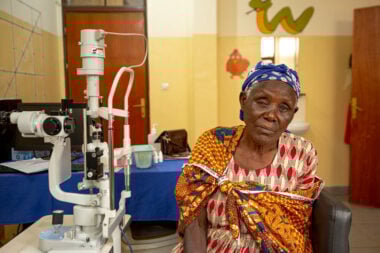 Valerie in a clinic with an eye examination machine beside her, wearing colourful clothes