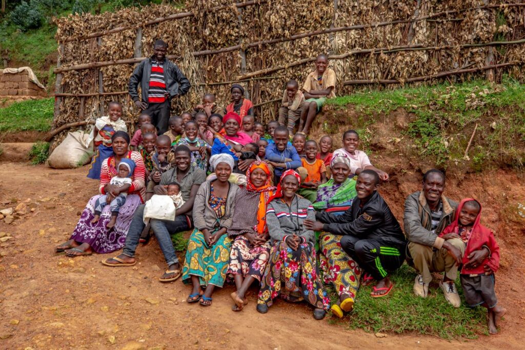 Velena sits outdoors, smiling, with a group of people celebrating her return to the community