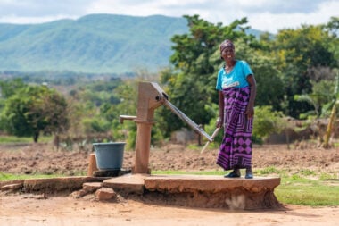 Mafunasi,wearing a blue t shirt, collects water using a pump. In the background are hills.