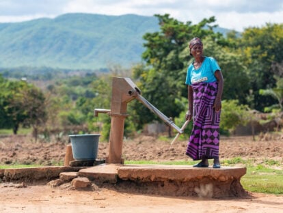 Mafunasi,wearing a blue t shirt, collects water using a pump. In the background are hills.
