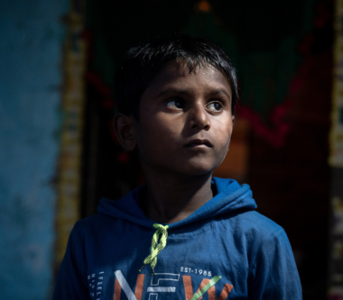A boy looks up to the right in a blue hoodie, his face partially lit by light.