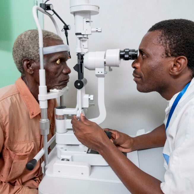 Dani, wearing a salmon shirt has his eyes examined by Vincent, an ophthalmologist.