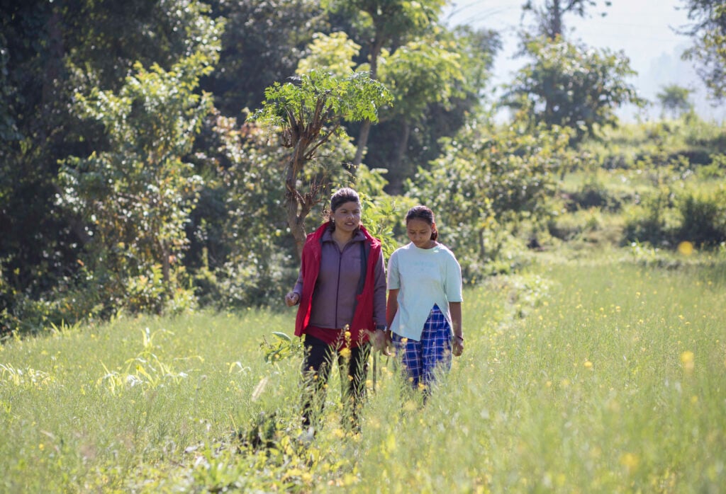 Someone, wearing a red CBM Jacket walks through a field alongside someone wearing white.