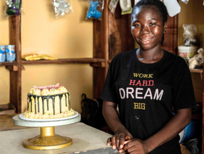 A girl smiles at the camera wearing a t-shirt that says Work Hard Dream Big, with a Birthday cake on the table next to her.