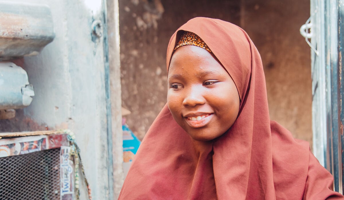 A teenage girl wearing a dark orange headscarf.