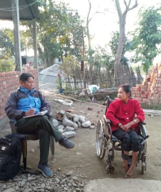 Ram Maya, sitting outside next to a man who is listening and taking notes.