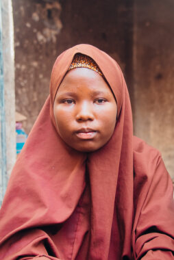 A Nigerian girl wearing a dark orange headscarf.