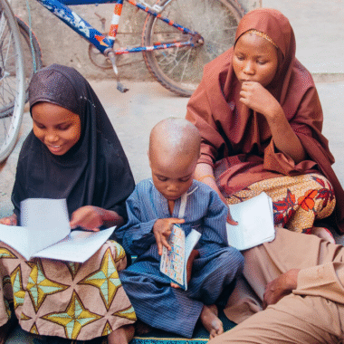 Three children sit on the ground looking at books.