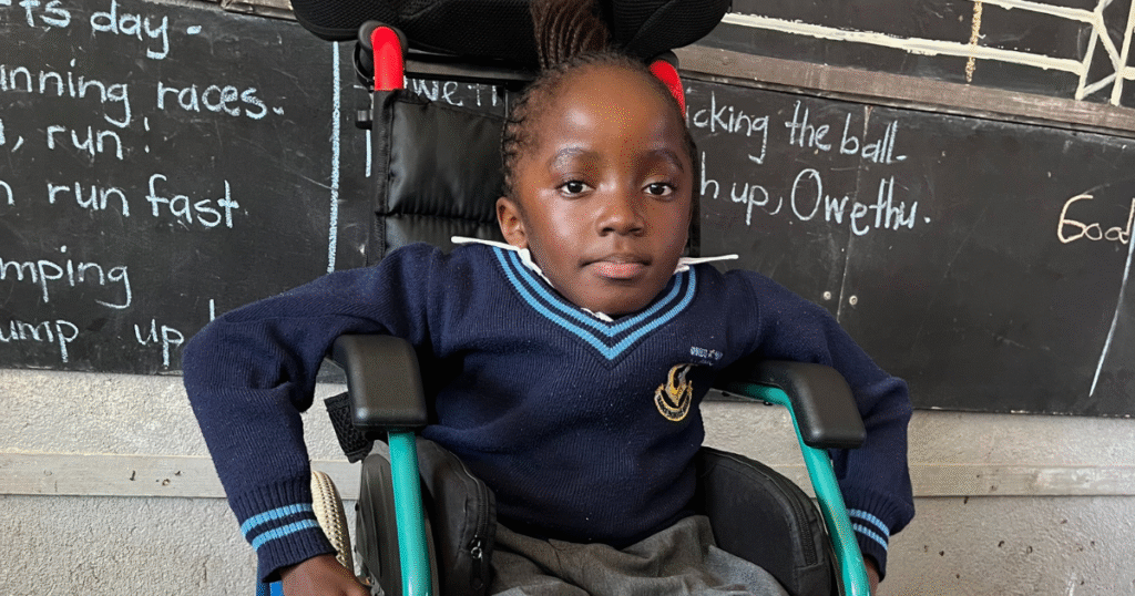 Kupa sitting in a wheelchair in front of a black board.