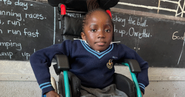 Kupa sitting in a wheelchair in front of a black board.