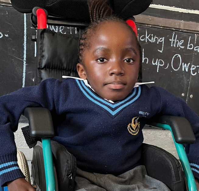 Kupa sitting in a wheelchair in front of a black board.