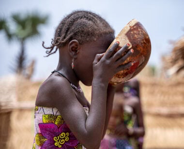 A young girl drinking from a bowl.