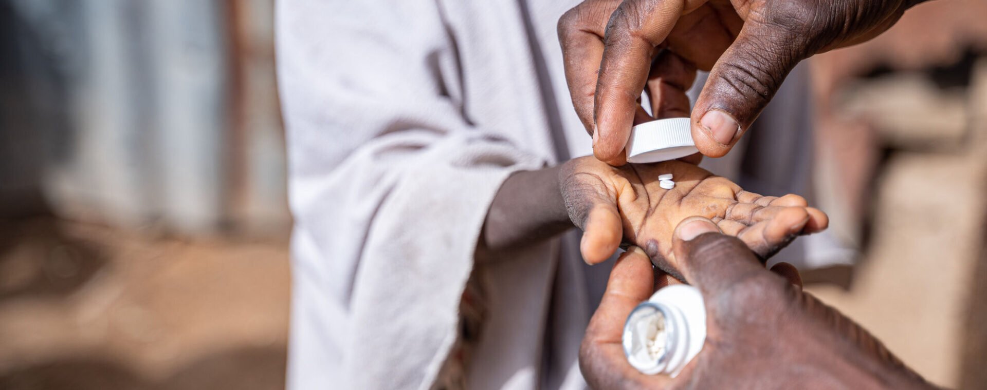 A pair of hands place some white tablets in a child's outstretched palm.