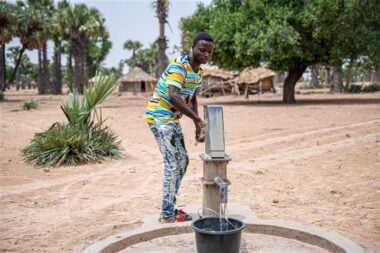 a man stood using a pump to draw water.
