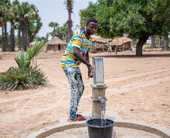 a man stood using a pump to draw water.