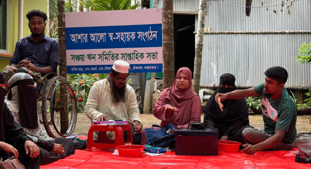 Members of a village savings and loans group in Bangladesh sit in a circle. One man leans over with some banknotes.