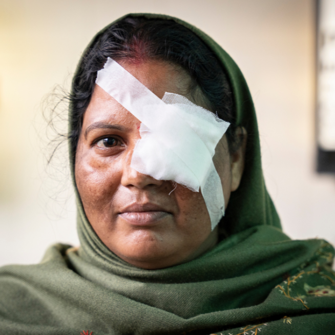A headshot of a lady wearing a green sari. She has a white bandage across her left eye.