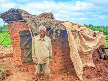 A man standing in front of a damaged brick hut.