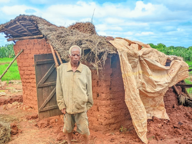 A man standing in front of a damaged brick hut.