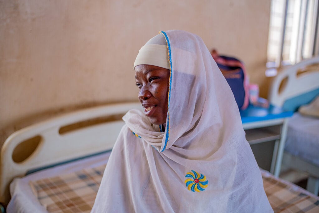 A young African woman in a white headscarf looks to the side with a smile on her face.