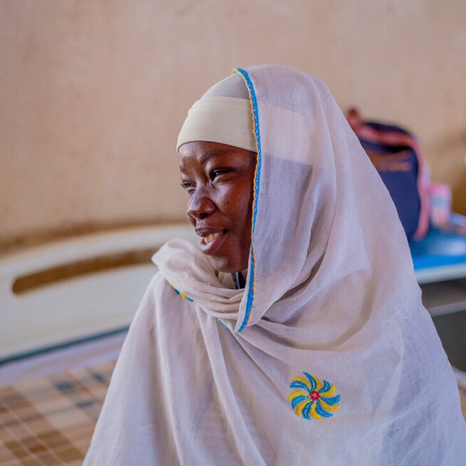 A young African woman in a white headscarf looks to the side with a smile on her face.