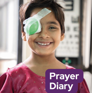 The cover of the CBM Prayer Diary, with a young Nepalese girl with short black hair, wearing a pink top. She has a green eye patch on her eye following cataract surgery and is smiling.