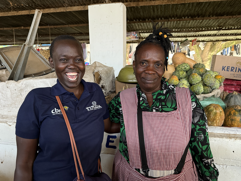 A CBM partner standing with a BasicNeeds project participant at her market stall.