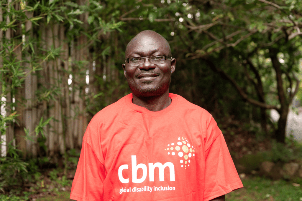Adrian Sakwa, wearing a CBM t-shirt, smiles at the camera.