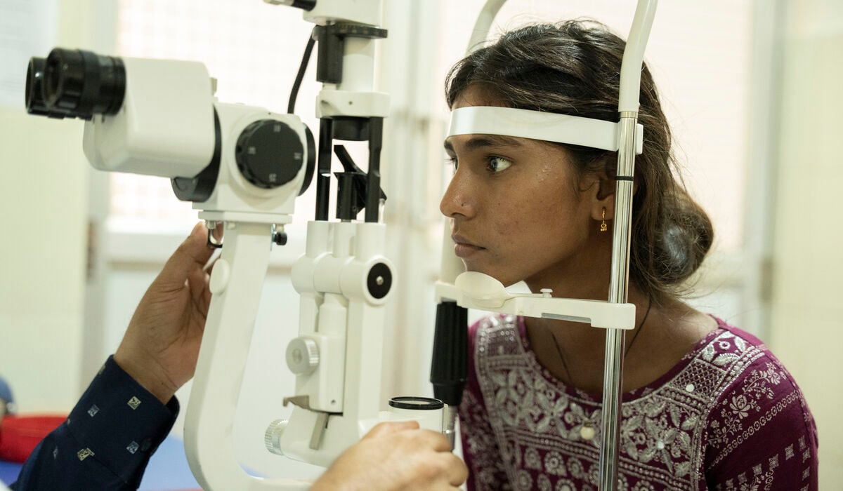 A Nepalese girl wearing a purple top, having her eyes examined with a machine in a clinic.