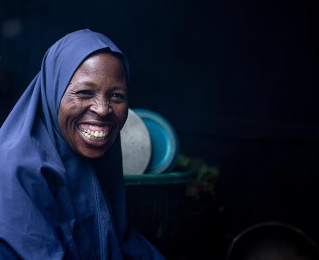 A woman in a blue headscarf smiles broadly towards the camera.