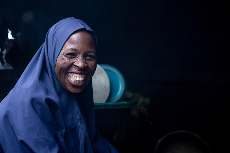 A woman in a blue headscarf smiles broadly towards the camera.