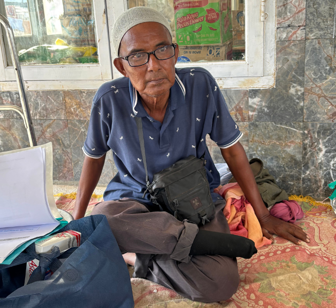A man is pictured sitting on the floor. He is sitting in an evacuation shelter after Indonesia Tropical Cyclone Senyar. He is wearing glasses and has a physical disability after having his leg amputated.