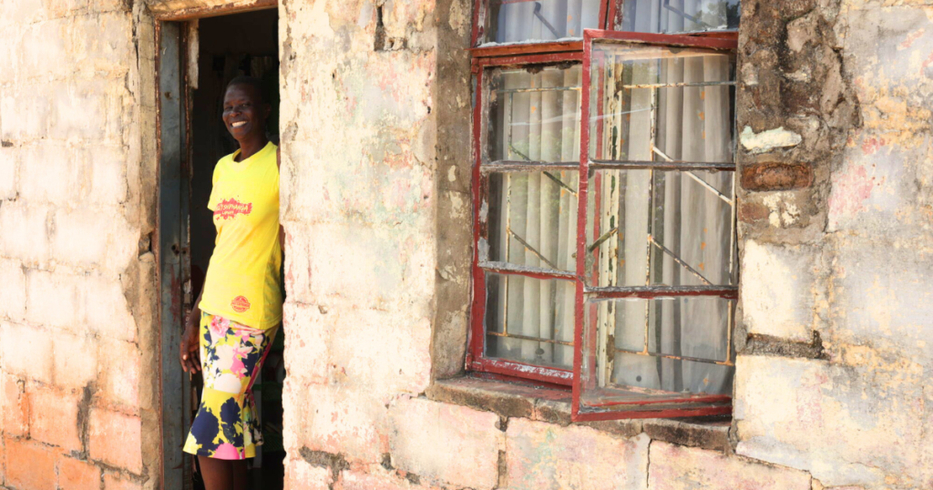A lady from Zimbabwe wearing a yellow t-shirt standing in a door way.