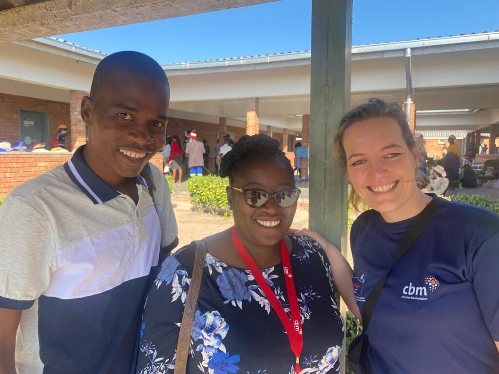 Three people stood outside a hospital in ZImbabwe, smiling into the camera.