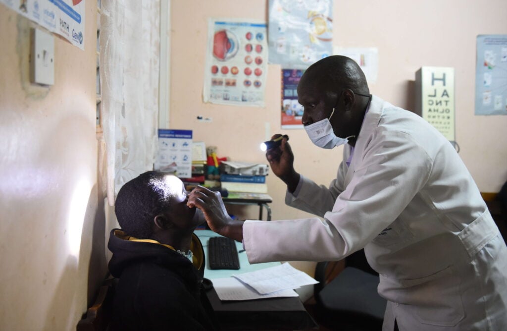 A doctor wearing a white coat shines a light into a patient's eye.