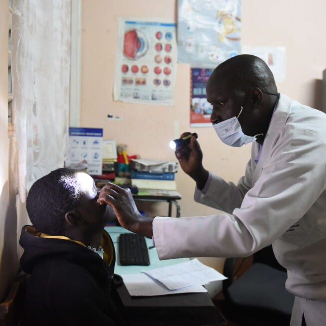 A doctor wearing a white coat shines a light into a patient's eye.
