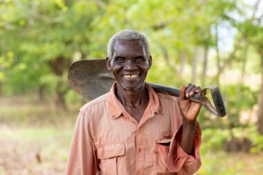 An elderly man is holding a spade
