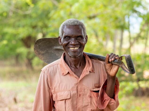 An elderly man is holding a spade