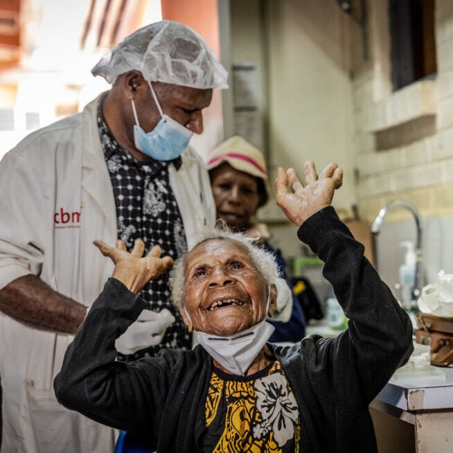 A lady waving her arms up in the arm following the removal of eye bandage. She can now see after cataract surgery.