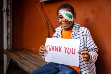 A young boy from PNG wearing an eye patch and holding a thank you sign.