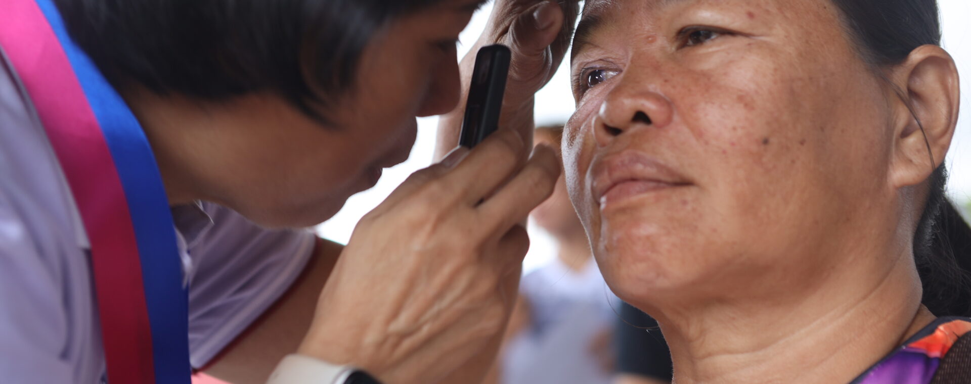 A woman has her eye inspected with an arclight.