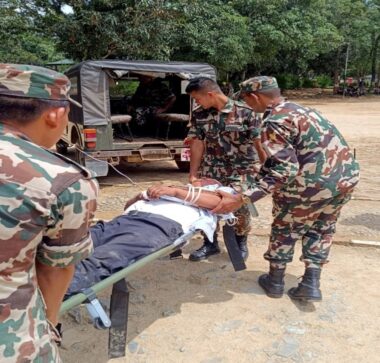 An elderly man on a stretcher being carried by army personnel across muddy flood water.