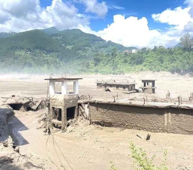 Buildings partially destroyed and covered in mud with mountains in the background.