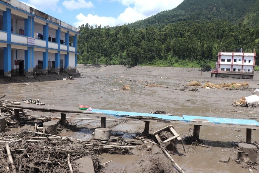 Flood-damaged buildings and muddy sediment covering the ground.