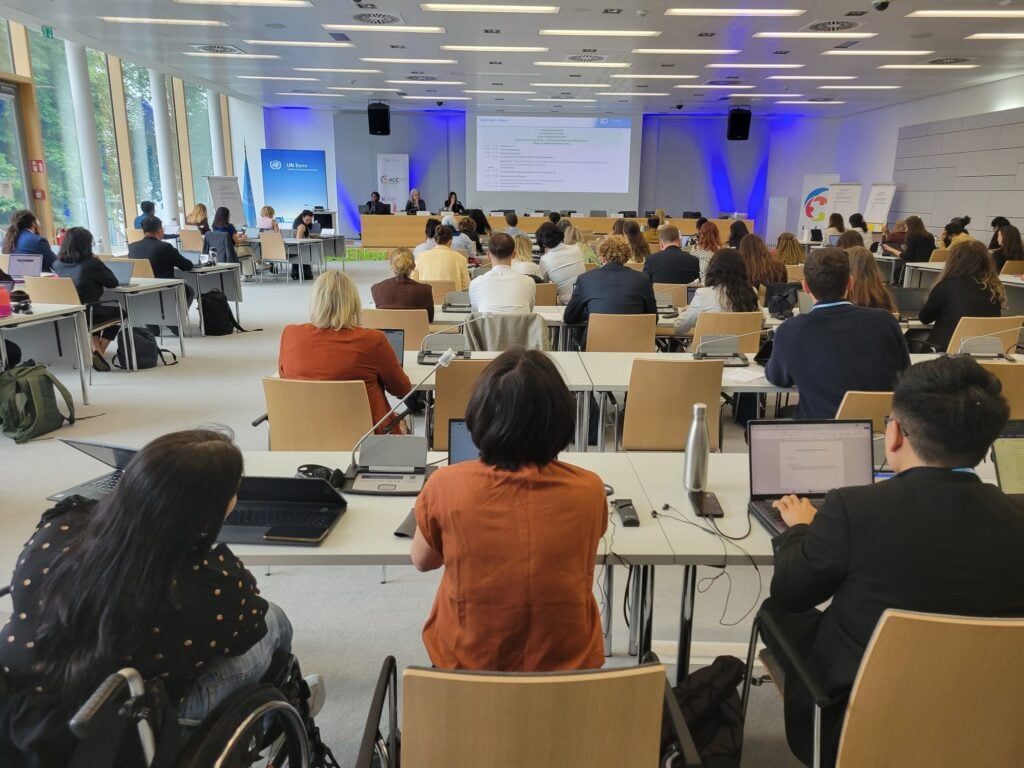 Participants at a workshop in Bonn sit behind desks and look towards a slide show projected at the front of the room.